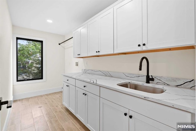 kitchen featuring light wood-style flooring, a sink, white cabinetry, and light stone countertops