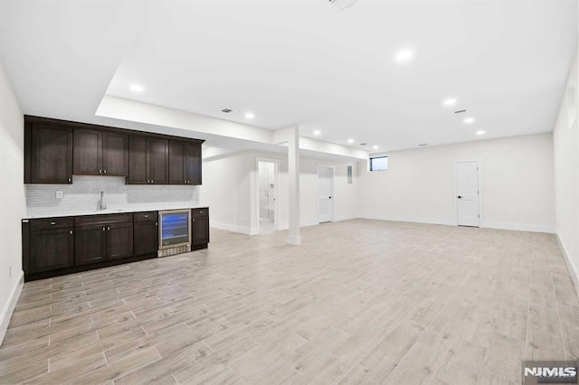 kitchen featuring beverage cooler, dark brown cabinetry, light wood-style flooring, and decorative backsplash