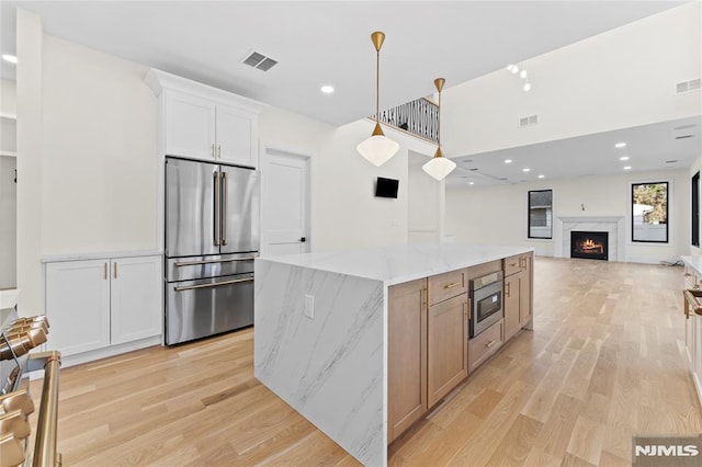 kitchen featuring light stone counters, a center island, visible vents, appliances with stainless steel finishes, and light wood-type flooring