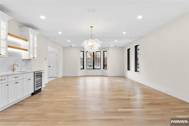 kitchen with white cabinets, decorative backsplash, wine cooler, light countertops, and light wood-style floors