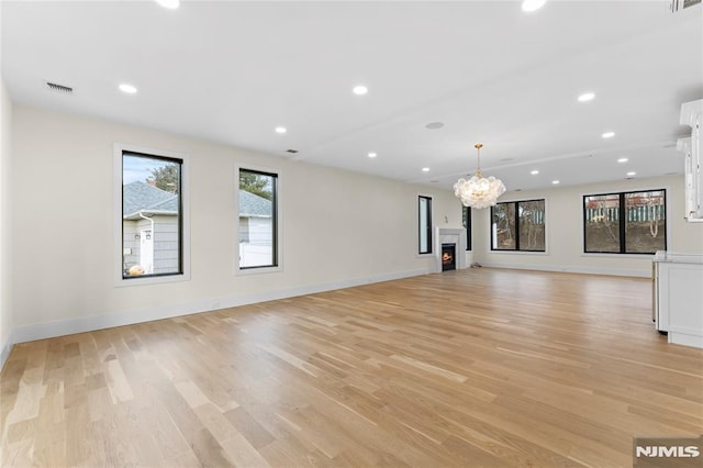 unfurnished living room with recessed lighting, a warm lit fireplace, visible vents, and light wood-style flooring