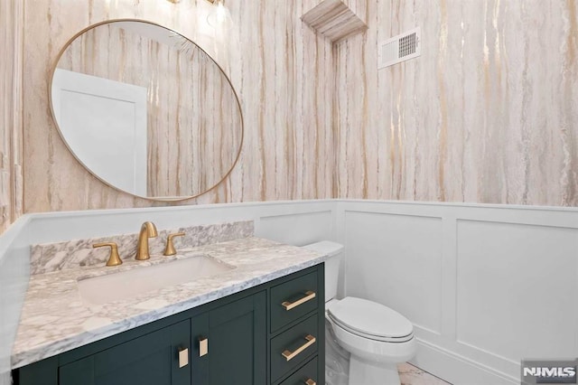 bathroom with marble finish floor, visible vents, a decorative wall, toilet, and vanity