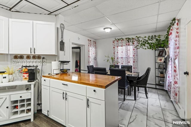 kitchen with a drop ceiling, a peninsula, butcher block counters, white cabinetry, and marble finish floor