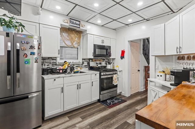 kitchen with appliances with stainless steel finishes, wood counters, white cabinetry, and decorative backsplash