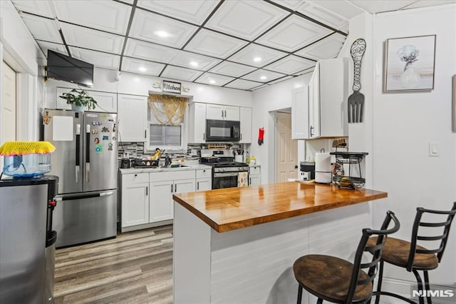 kitchen featuring a peninsula, white cabinetry, wooden counters, appliances with stainless steel finishes, and decorative backsplash