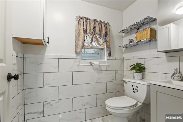 bathroom featuring toilet, marble finish floor, tile walls, and vanity