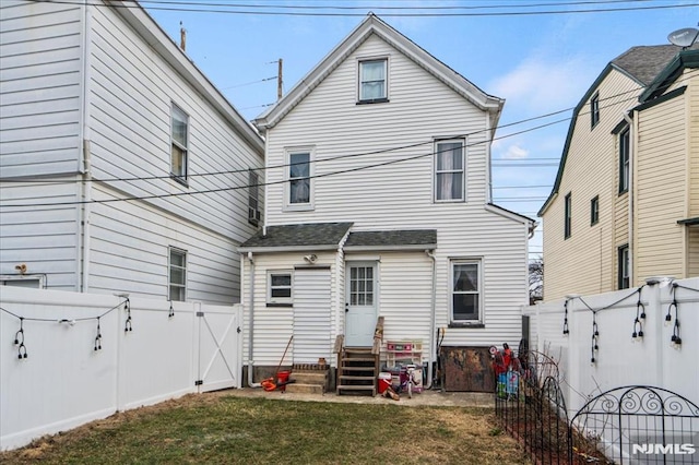 rear view of house with entry steps, a gate, a fenced backyard, and a yard