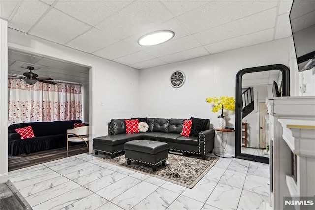 living area featuring marble finish floor, ceiling fan, and a drop ceiling