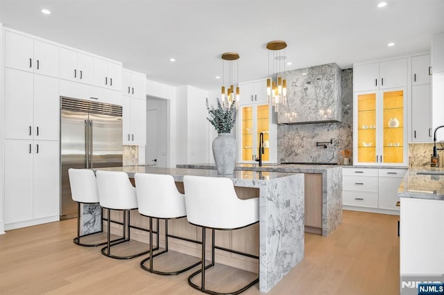 kitchen featuring a sink, built in refrigerator, a kitchen island, and light wood-style flooring