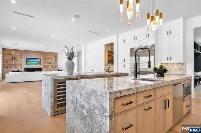 kitchen featuring a fireplace, a center island with sink, light wood-style floors, a sink, and beverage cooler