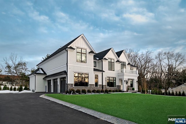 view of front facade featuring an attached garage, board and batten siding, a front yard, a balcony, and stone siding