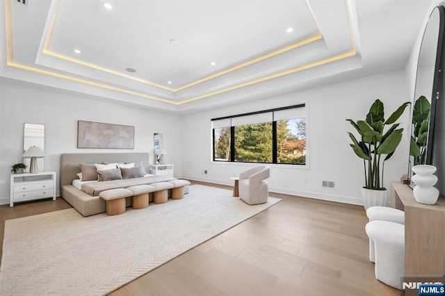 bedroom featuring a raised ceiling, visible vents, baseboards, and wood finished floors