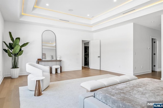 bedroom featuring stacked washer and dryer, wood finished floors, a raised ceiling, and baseboards