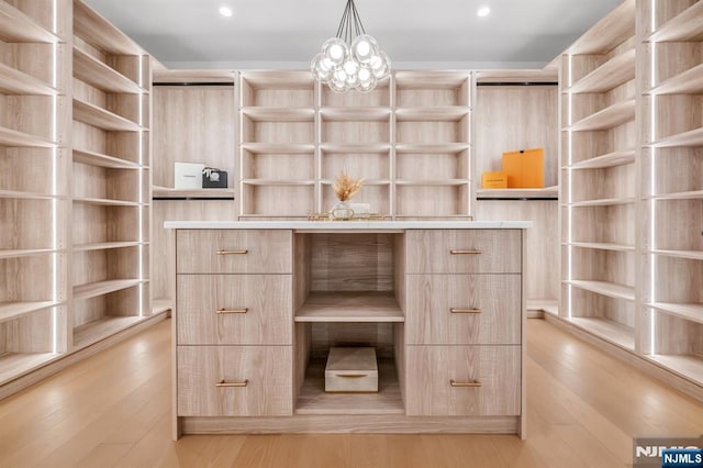 walk in closet with light wood finished floors and a notable chandelier