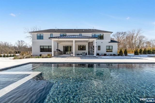 back of property with metal roof, a standing seam roof, a patio area, and an outdoor pool