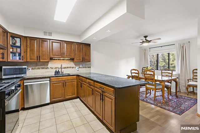 kitchen featuring visible vents, decorative backsplash, appliances with stainless steel finishes, a peninsula, and a sink