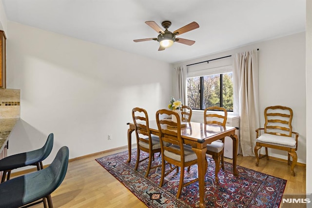 dining space with ceiling fan, baseboards, and light wood-style flooring