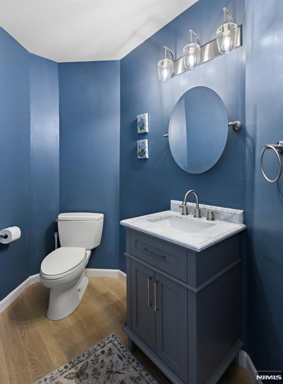 half bathroom with vanity, toilet, wood finished floors, and baseboards