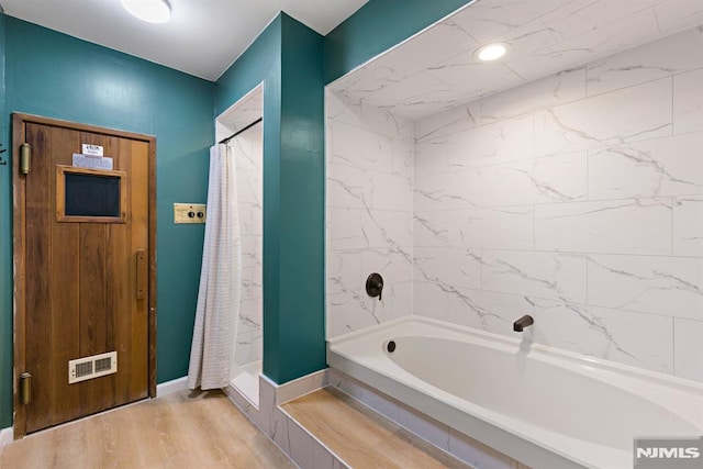 full bath with visible vents, a washtub, a shower with shower curtain, and wood finished floors