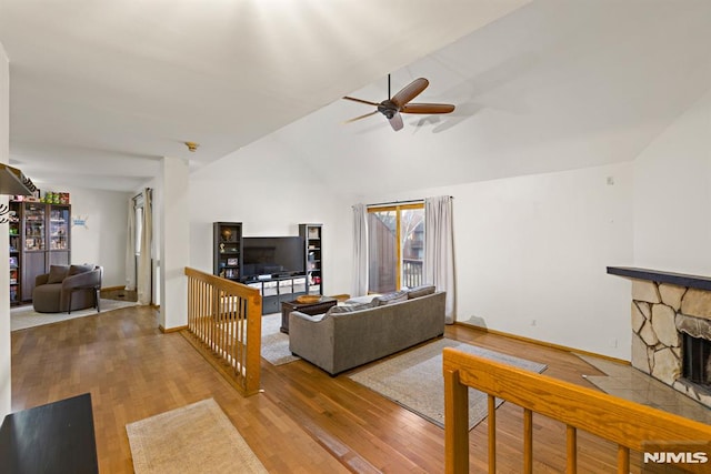 living area with baseboards, lofted ceiling, a fireplace, wood finished floors, and a ceiling fan