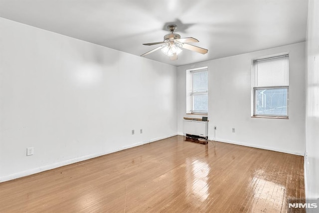 empty room featuring a ceiling fan, radiator, baseboards, and hardwood / wood-style flooring