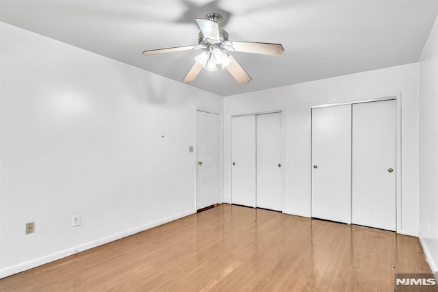 unfurnished bedroom with baseboards, wood finished floors, a ceiling fan, and multiple closets