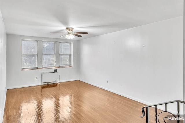 empty room with radiator, wood-type flooring, baseboards, and a ceiling fan