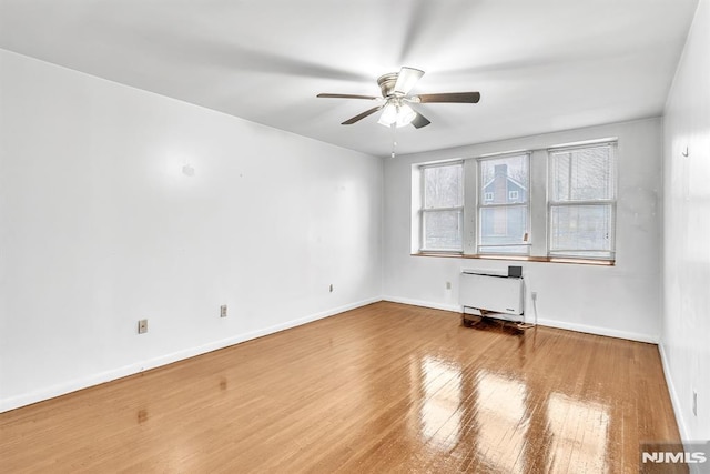 spare room featuring heating unit, wood-type flooring, baseboards, and ceiling fan