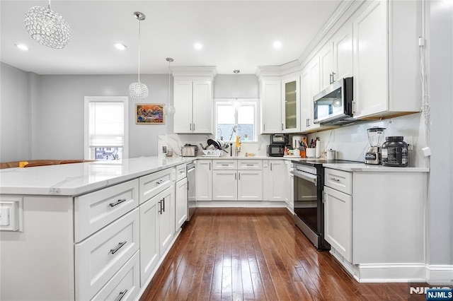 kitchen with light stone counters, dark wood-style floors, appliances with stainless steel finishes, a peninsula, and white cabinets