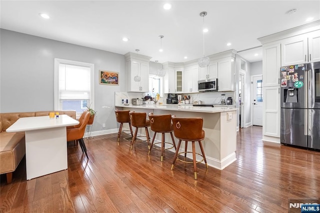 kitchen with dark wood finished floors, a peninsula, stainless steel appliances, and a kitchen bar