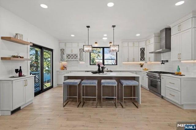 kitchen with a breakfast bar, a kitchen island, light wood-style floors, high end range, and wall chimney exhaust hood