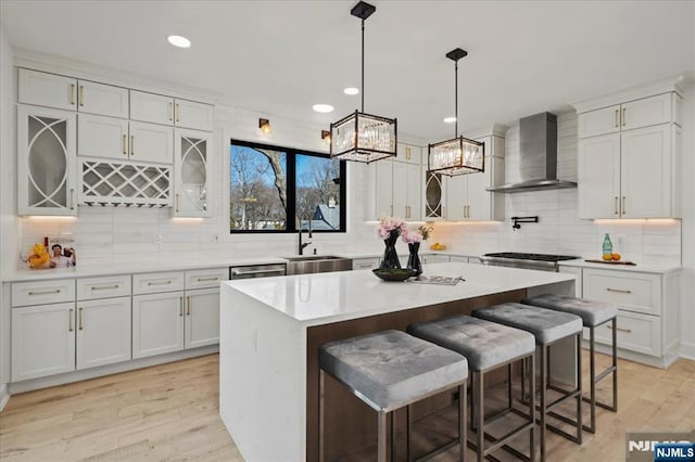 kitchen featuring a sink, a kitchen breakfast bar, light countertops, wall chimney exhaust hood, and light wood finished floors