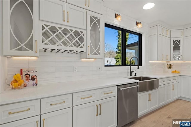 kitchen featuring a sink, white cabinets, light countertops, stainless steel dishwasher, and backsplash