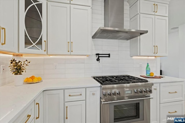 kitchen featuring high end stove, white cabinetry, wall chimney range hood, and backsplash