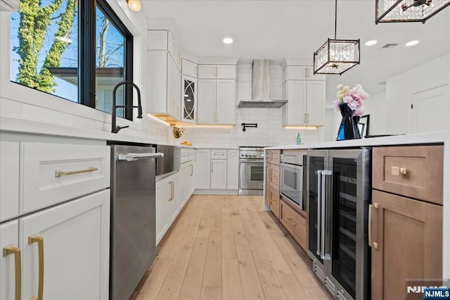 kitchen featuring oven, beverage cooler, light countertops, wall chimney range hood, and tasteful backsplash