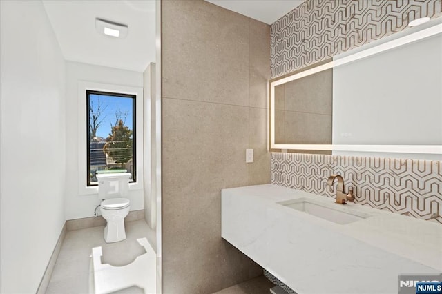 bathroom with baseboards, toilet, tile patterned floors, a sink, and tile walls