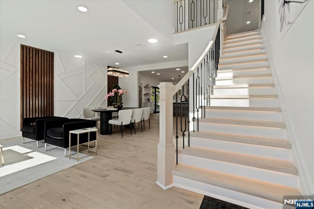 stairs with a decorative wall, wood finished floors, and recessed lighting