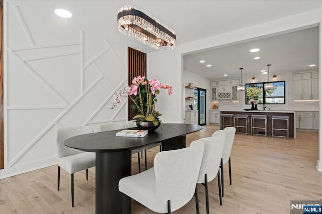 dining room featuring a chandelier, light wood finished floors, recessed lighting, and a decorative wall