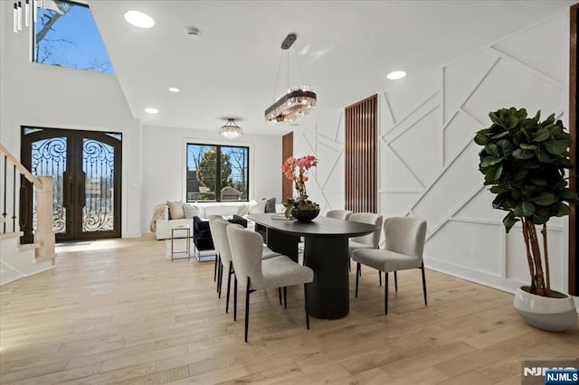 dining area featuring light wood-type flooring, stairway, a decorative wall, and french doors