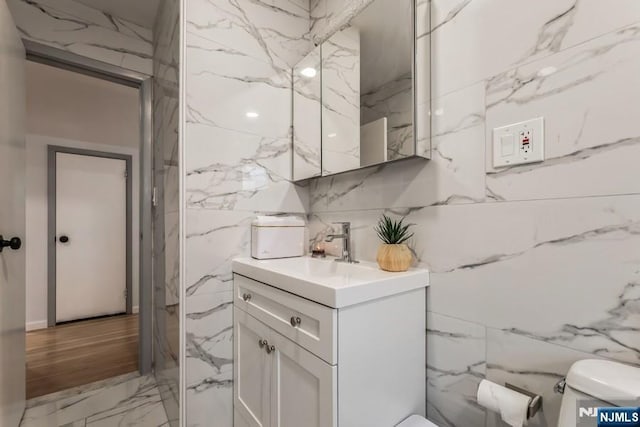 half bath with toilet, stone wall, marble finish floor, and vanity