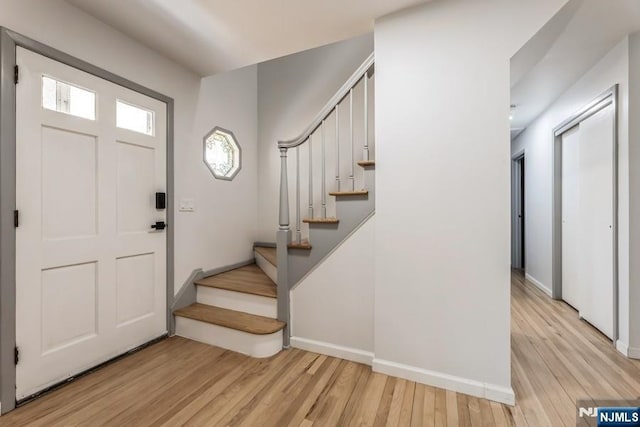 foyer entrance featuring light wood finished floors, stairs, and baseboards