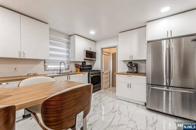 kitchen with white cabinets, appliances with stainless steel finishes, a sink, marble finish floor, and backsplash