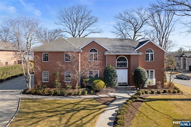 view of front of house featuring driveway, brick siding, and a front lawn