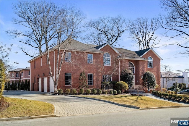 view of front of house featuring decorative driveway, brick siding, an attached garage, and a front lawn