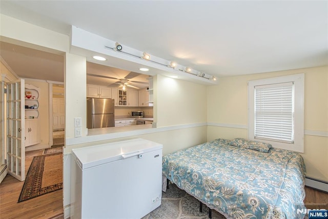 bedroom with refrigerator, a baseboard heating unit, wood finished floors, and freestanding refrigerator