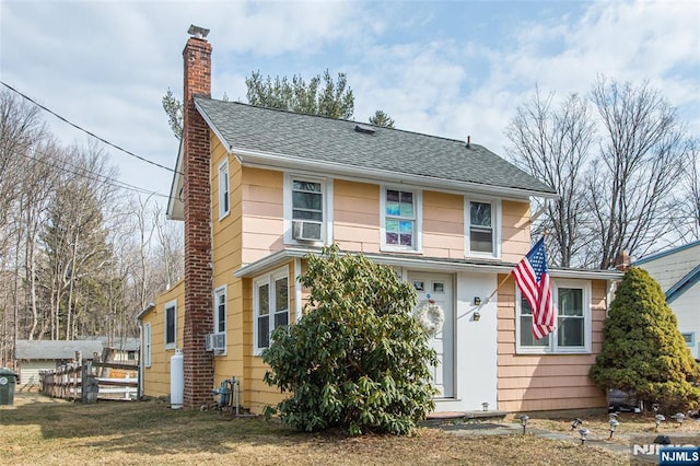 view of front facade featuring a shingled roof, cooling unit, a chimney, and a front yard