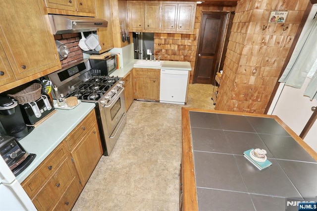 kitchen featuring white dishwasher, a sink, black microwave, under cabinet range hood, and stainless steel gas range oven