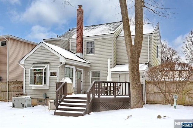 snow covered house featuring a deck, crawl space, a chimney, and fence