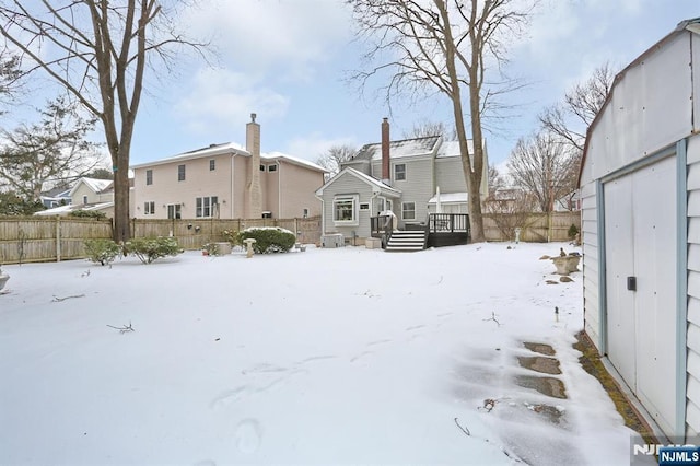 snow covered house featuring a fenced backyard, a residential view, and a wooden deck