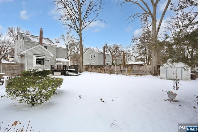 snowy yard with a fenced backyard, a storage unit, a wooden deck, and an outbuilding